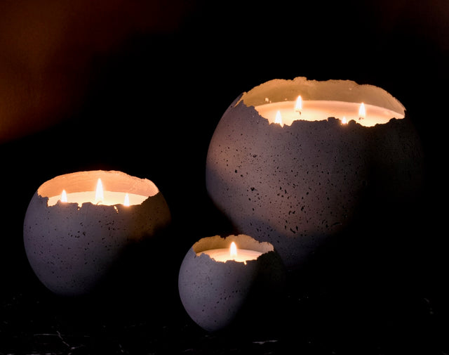 Three concrete Orbis candle holders with lit candles on a dark background. Medium, large and XL in charcoal