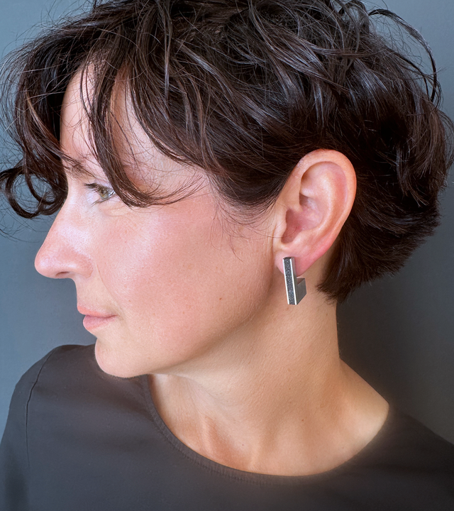 A model wears a modern geometric stainless steel stud earring with a concrete-and-diamond dust inlay— inspired by the minimalist Bauhaus design principles of Anni Albers.