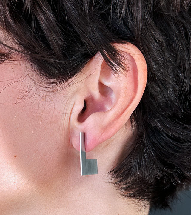 Close-up of model's ear featuring minimalist geometrical shaped stainless steel stud earring inspired by Bauhaus designer Anni Albers.
