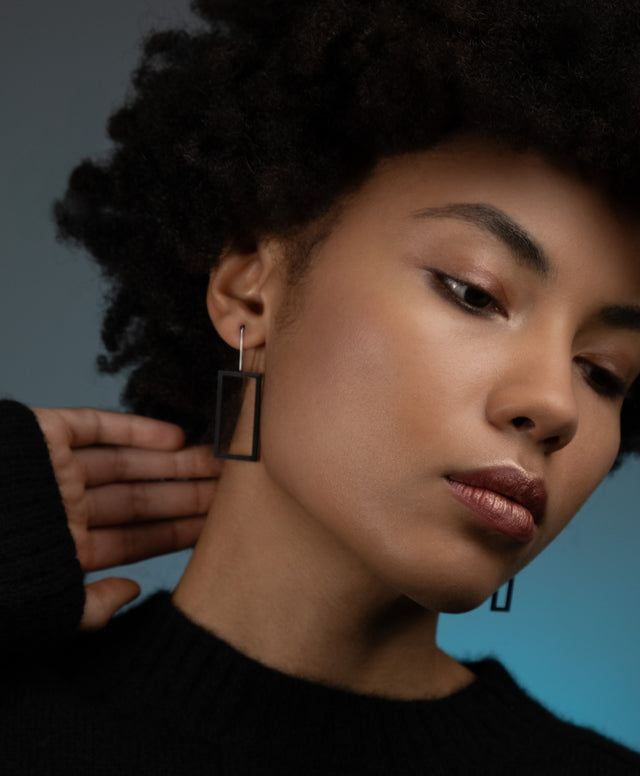a model wearing minimalist rectangular black powder coated drop earrings from the KONZUK Artus collection