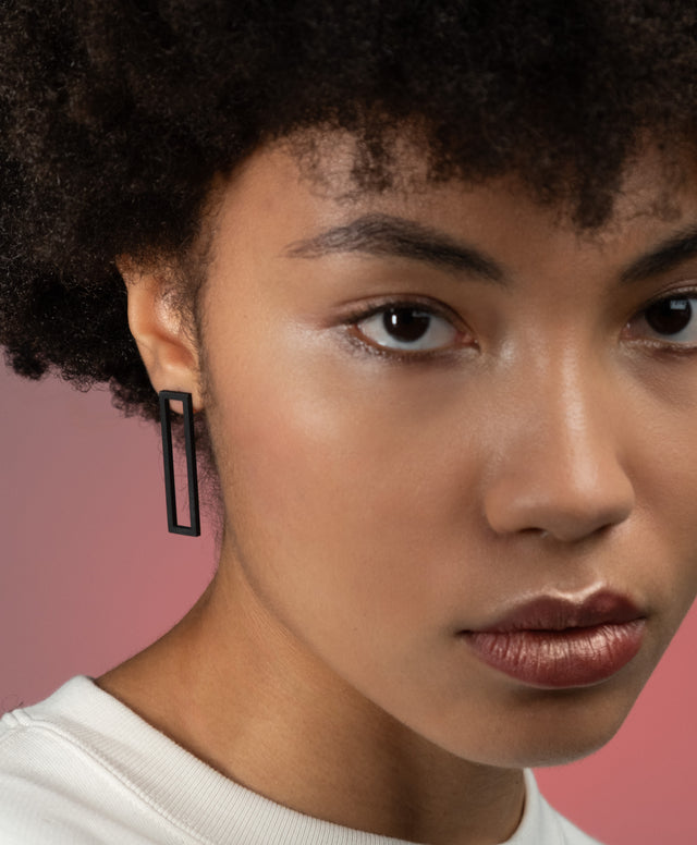 a model wearing a pair of black powder coated long rectangular studs from the KONZUK Artus collection