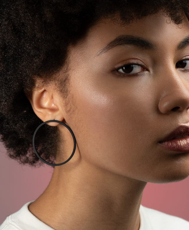 a woman wearing a simple yet bold pair of statement hoop earrings of black powder coated stainless steel from the KONZUK Artus collection.