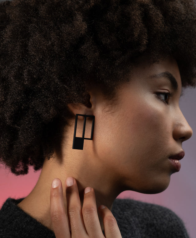 A woman wearing a black powder coated stainless steel rectangular earring which is geometric in style from the Artus collection.