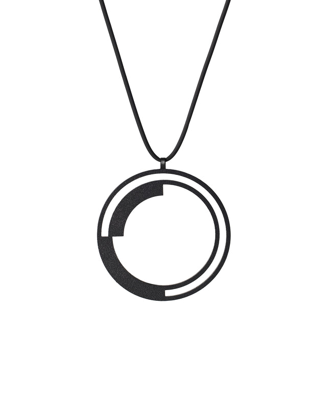 This pendant introduces curves into the collection's vocabulary, creating a rhythmic balance as the solid forms anchor the circular form while leaving generous arcs of openness between them. The double-ring structure adds depth and layering, transforming the simple circle into a study of rotation and counterbalance. It's a dynamic composition that suggests movement and continuity, as if the solid arcs are in gentle orbit within their circular bounds.