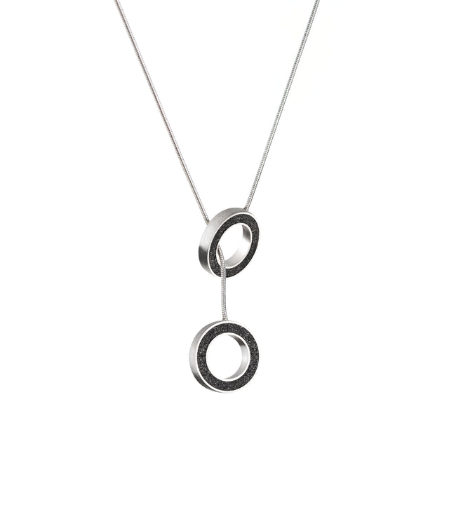 Two circular pendants with black diamond dust orbit on a stainless steel lariat chain. Celestial-inspired, minimalist KONZUK jewelry design.