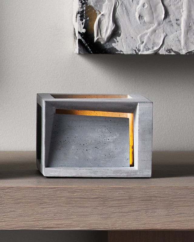 The Pavilion is a minimalist concrete tea light holder that transforms a simple candle into an architectural statement piece. Crafted with layers of raw concrete it casts dramatic light and shadow patterns that create instant ambiance in any room. Its brutalist aesthetic adds sophisticated, gallery-worthy style to your space while providing warm, intimate lighting perfect for relaxation or entertaining. 