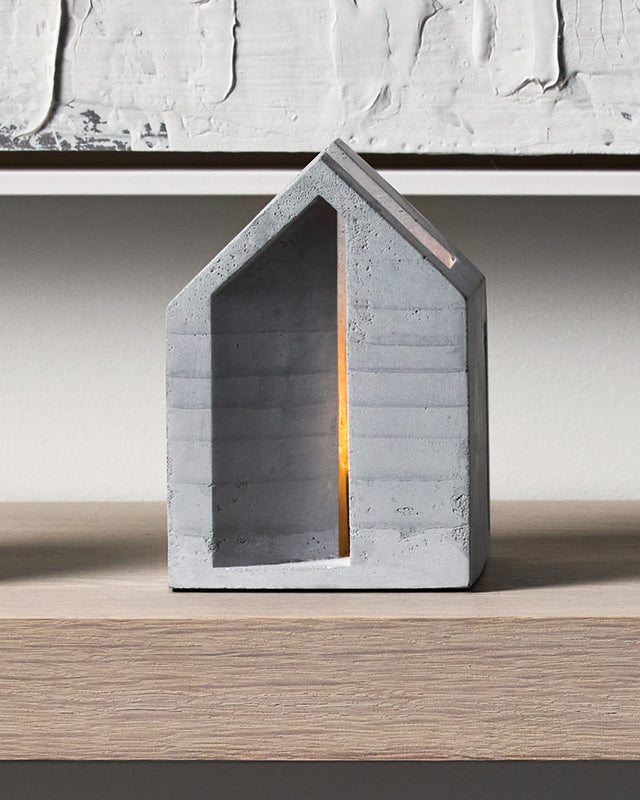 Light streams through a slender portal beneath a peaked roof, while a clerestory window offers a second glimpse into this concrete sanctuary's illuminated interior. Each holder includes a cork base to protect surfaces.