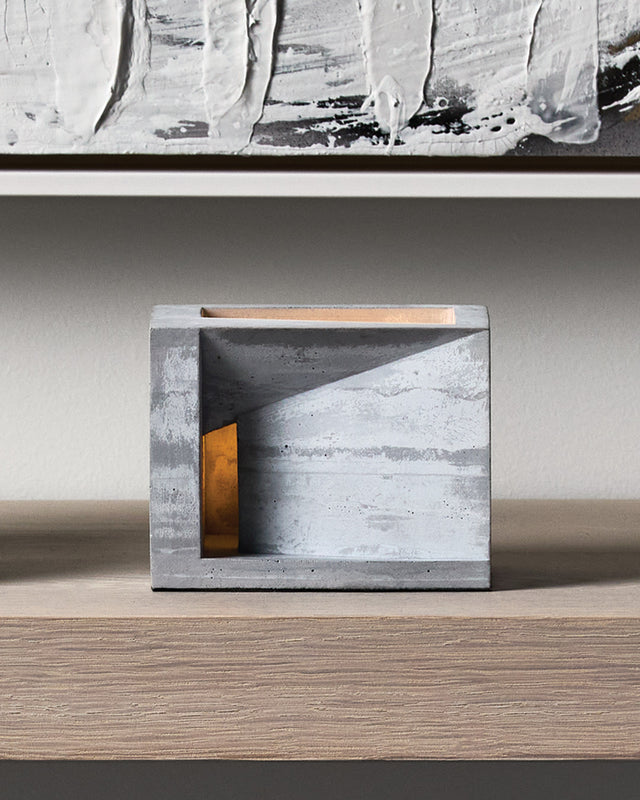 Villa is a concrete tea light holder that reveals the beautiful layered striations of cast concrete, like geological strata that tell the story of its creation. With its cubic architecture and generous rectangular opening, the candlelight illuminates these textured layers from within, offering an intimate glimpse into the imagined life of its inhabitant—as if peering through a window into a warm, lived-in space. This sculptural piece brings contemplative depth and serene ambiance to your home, transforming
