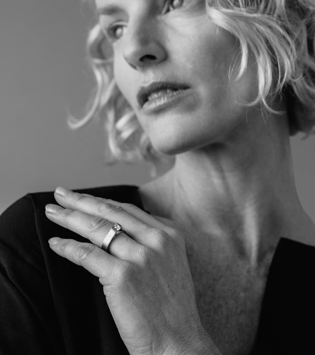 a model wearing This ring showcases a striking minimalist design, featuring a half-carat diamond elegantly suspended within a sculptural band. Its clean, modern form highlights precision craftsmanship and architectural balance. Available in stainless steel, platinum, or a platinum and gold combination, this piece embodies refined simplicity and timeless strength.