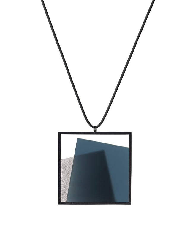 The Astrid necklace in cerulean blue takes its name from Old Norse, meaning “divinely beautiful,” a reflection of its quiet, sculptural presence. Within the square frame, concrete intersects with resin in a deliberate composition that reveals depth and movement. The meeting of materials creates subtle shifts in tone and surface, drawing the eye to the balance between precision and softness. The Astrid necklace embodies refined minimalism with a sense of calm, architectural beauty.