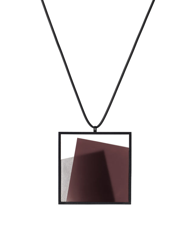 The Astrid necklace in cognac takes its name from Old Norse, meaning “divinely beautiful,” a reflection of its quiet, sculptural presence. Within the square frame, concrete intersects with resin in a deliberate composition that reveals depth and movement. The meeting of materials creates subtle shifts in tone and surface, drawing the eye to the balance between precision and softness. The Astrid necklace embodies refined minimalism with a sense of calm, architectural beauty.