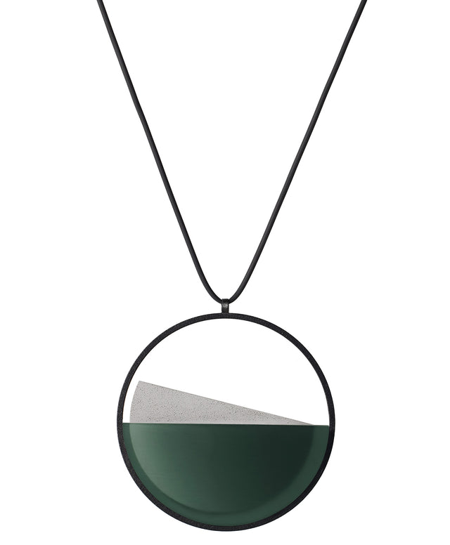 The Clara necklace in cypress green resin embodies clarity and balance. Named from the Latin clarus, meaning “bright” or “clear,” it reflects the quiet harmony of light and material. Within the circular frame, concrete emerges from the surface of the resin, creating a gentle rise in tone and texture. The Clara necklace carries a calm, sculptural presence that feels both modern and enduring.