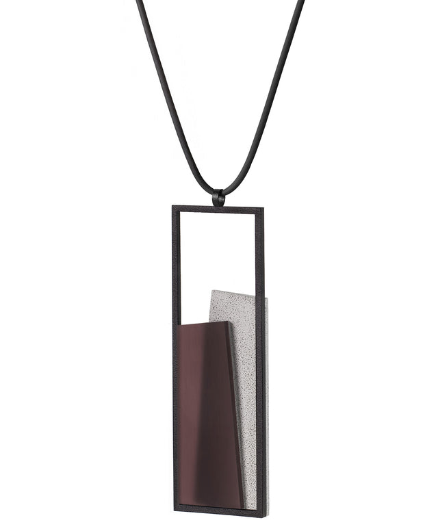 Side view of The Eira in Cognac resin necklace brings together concrete and resin in a seamless composition that highlights material depth and subtle tone. Within the black rectangular frame, the concrete appears softly suspended in resin, giving the piece a quiet sense of balance and dimension. The surface catches light in a gentle, diffused way, creating an effect that feels both grounded and luminous. The Eira necklace offers a refined expression of modern minimalism.