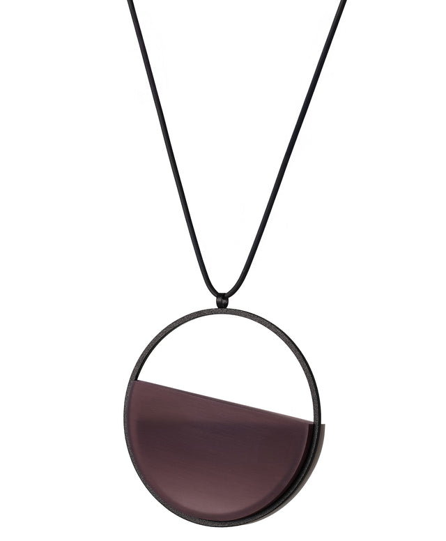 side view of The Vestra necklace in Cognac resin embodies balance and quiet strength. Its name, derived from the Latin vestra, meaning “yours,” speaks to a personal connection between wearer and form. Within the circular frame, concrete is cast into resin revealing a smooth plane of depth and tone, reflecting light in a soft, fluid way. The composition feels calm and grounded, offering a sculptural presence that becomes uniquely individual when worn.
