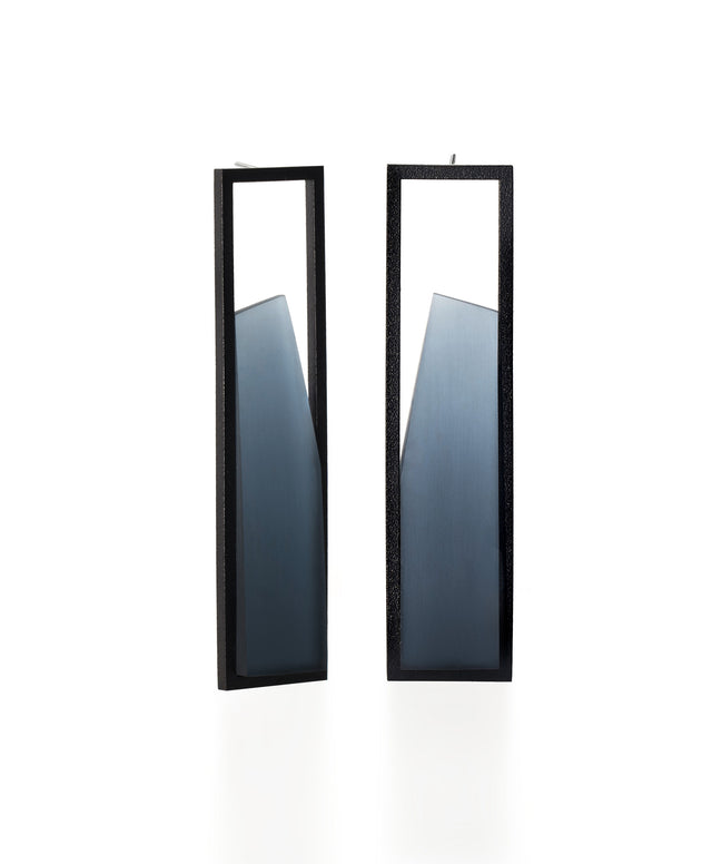 The Lucia earrings feature a sculptural interplay of shadow and light within a sleek rectangular frame. As the wearer moves, the translucent insets shift in tone deepening and softening with a turn of the head. Their geometric form captures a quiet elegance, embodying the Lumina Collection’s exploration of contrast and depth. A refined statement piece that is guaranteed to draw the eye. available in cerulean blue