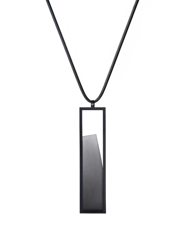 The Lucia necklace in Ash grey resin features a sleek rectangular pendant that emphasizes form and material. A cast resin element rests within a black frame, creating a sense of depth and quiet luminosity. The elongated shape draws the eye, offering a refined balance between structure and softness. Minimal and striking, the Lucia necklace adds a sculptural accent that complements both everyday and statement looks.