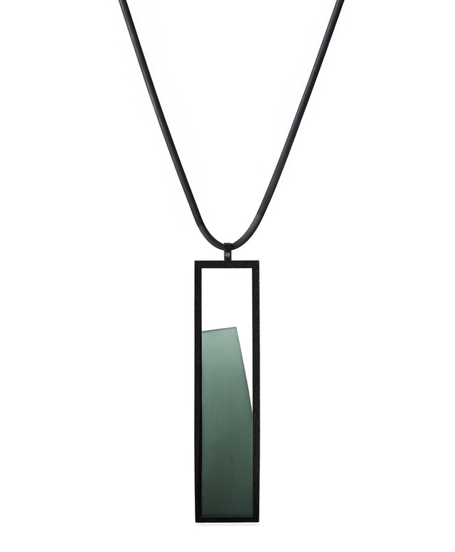 The Lucia necklace in Cypress Green features a sleek rectangular pendant that emphasizes form and material. A cast resin element rests within a black frame, creating a sense of depth and quiet luminosity. The elongated shape draws the eye, offering a refined balance between structure and softness. Minimal and striking, the Lucia necklace adds a sculptural accent that complements both everyday and statement looks.