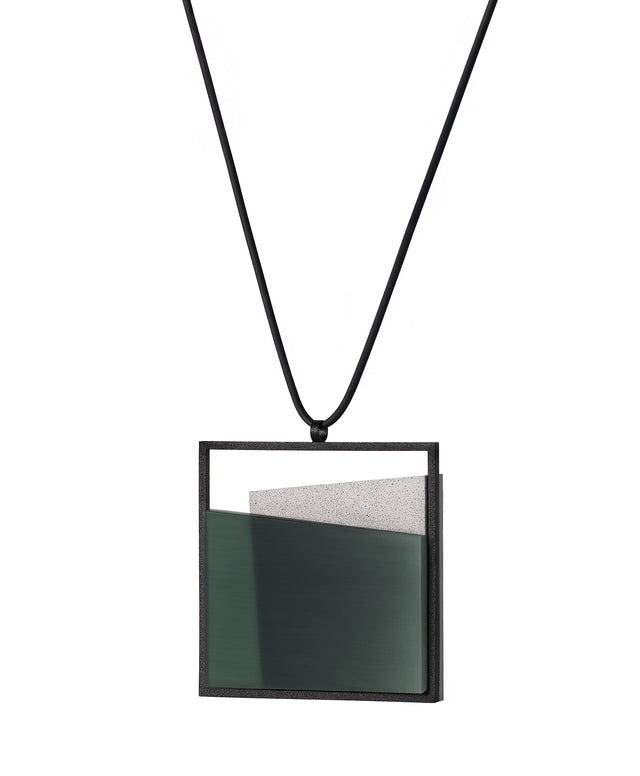 side view of The Mara necklace in cypress green evokes stillness, and movement within form. Concrete is cast into resin inside a square frame, where the materials meet in a smooth, fluid line. The surface reflects light with quiet subtlety, creating the sense of horizon and depth. The Mara necklace embodies balance and serenity through modern, sculptural design.