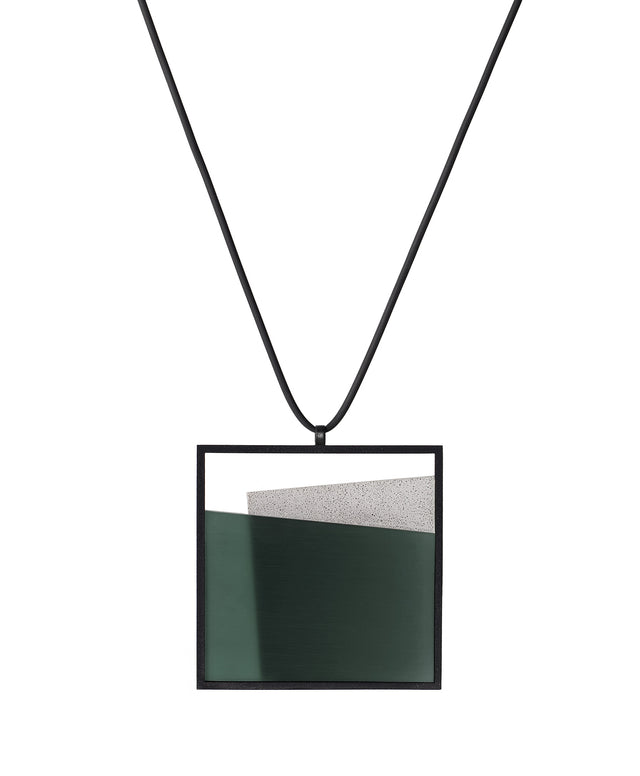 The Mara necklace in cypress green resin evokes depth, stillness, and movement within form. Concrete is cast into resin inside a square frame, where the materials meet in a smooth, fluid line. The surface reflects light with quiet subtlety, creating the sense of horizon and depth. The Mara necklace embodies balance and serenity through modern, sculptural design.