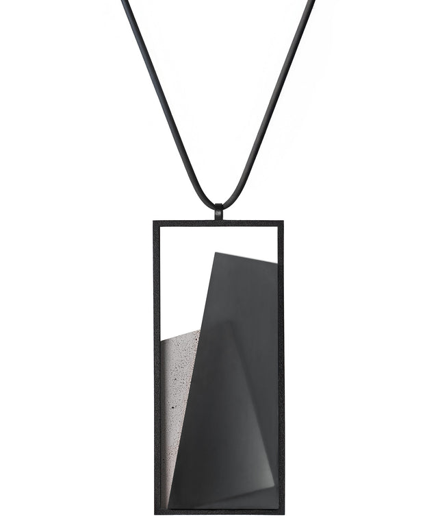 The Naia necklace in Ash grey embodies the feeling of wearing a work of art. Within its black rectangular frame, layers of resin and concrete are composed with sculptural precision, creating depth and quiet movement. The graduated tone of the resin shifts gently with the light, giving the piece a quiet, sculptural presence. Balanced and distinctive, the Naia necklace transforms simple geometry into a refined expression of wearable art.