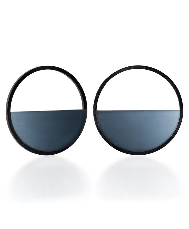 The Sola earrings feature a bold circular form that highlights the depth and tone of cast resin. Larger in scale, they create a sculptural statement while maintaining a sense of balance and simplicity. The smooth surface holds a quiet luminosity that contrasts beautifully with the dark frame, giving the design a modern yet understated presence. IN CERULEAN BLUE
