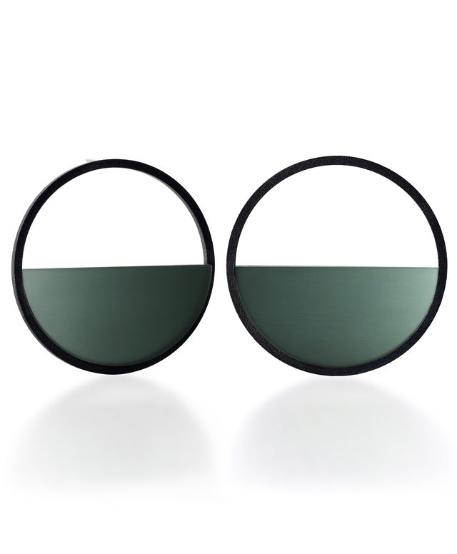 The Sola earrings feature a bold circular form that highlights the depth and tone of cast cypress green resin. Larger in scale, they create a sculptural statement while maintaining a sense of balance and simplicity. The smooth surface holds a quiet luminosity that contrasts beautifully with the dark frame, giving the design a modern yet understated presence.