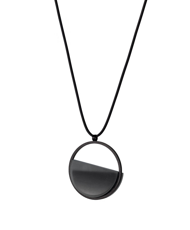 side version of the ash grey Vestra Small necklace captures the same sense of balance and quiet strength in a more understated form that the larger version. Named from the Latin vestra, meaning “yours,” it reflects a personal connection between light, material, and wearer. The smaller circular frame holds a smooth resin plane with a cast concrete inset that reveals gentle depth and tone, creating a soft glow close to the body. 