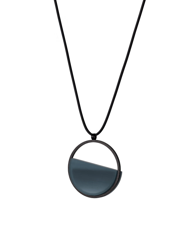 The side version of the Vestra Small necklace in cerulean blue resin captures the same sense of balance and quiet strength in a more understated form that the larger version. Named from the Latin vestra, meaning “yours,” it reflects a personal connection between light, material, and wearer. The smaller circular frame holds a smooth resin plane with a cast concrete inset that reveals gentle depth and tone, creating a soft glow close to the body.