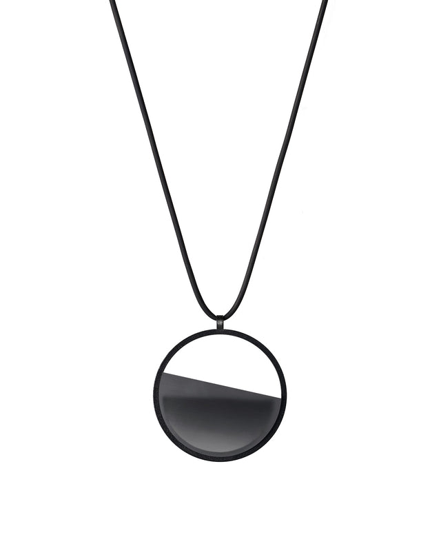 The Vestra Small necklace captures the same sense of balance and quiet strength in a more understated form that the larger version. Named from the Latin vestra, meaning “yours,” it reflects a personal connection between light, material, and wearer. The smaller circular frame holds a smooth resin plane with a cast concrete inset that reveals gentle depth and tone, creating a soft glow close to the body