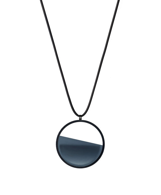 The Vestra Small necklace in cerulean blue resin captures the same sense of balance and quiet strength in a more understated form that the larger version. Named from the Latin vestra, meaning “yours,” it reflects a personal connection between light, material, and wearer. The smaller circular frame holds a smooth resin plane with a cast concrete inset that reveals gentle depth and tone, creating a soft glow close to the body.