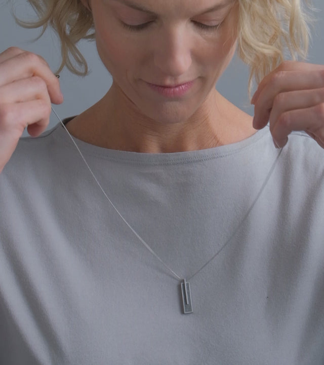 Video of model wearing Memento Beholden pendent with diamond dust concrete set into small rectangular stainless steel design.