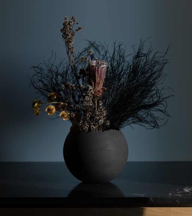 Hand-crafted black concrete vessel with a live-edge opening, designed for use as a planter. with a dried floral arrangement
