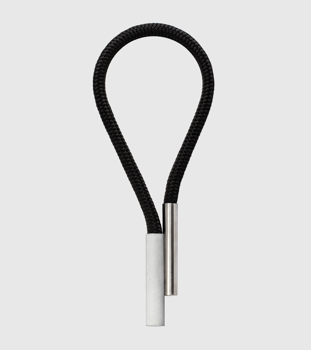 A minimalist-designed statement piece featuring a black satin nylon rope, a concrete cylinder, and a stainless steel cylinder with a brushed finish, held together by rare-earth magnets.