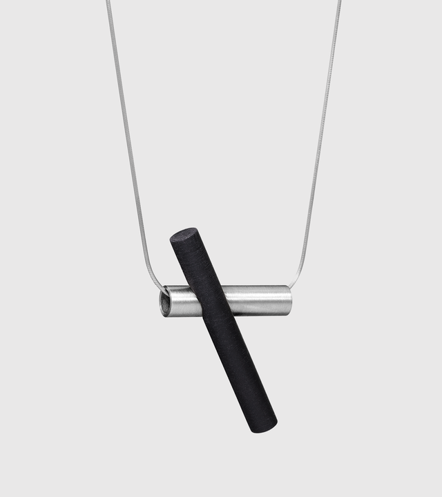 Suspended from a stainless steel snake chain a black-tinted concrete cylinder cantilevers a brushed stainless steel tube.