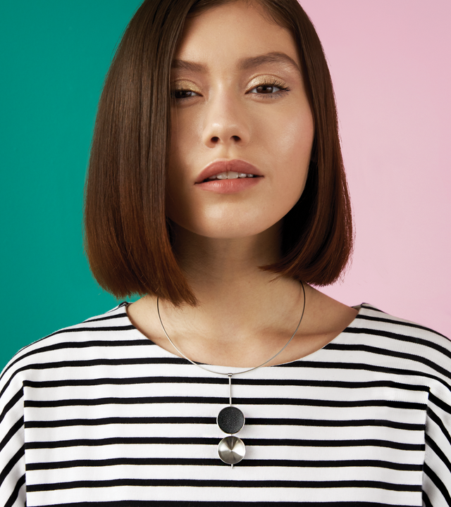 The Bauhaus inspired Freya necklace features two larger double stainless steel domes, one lined with the sparkle of diamond dust infused black concrete both architecturally supported by an elegant hanging steel post and cable.