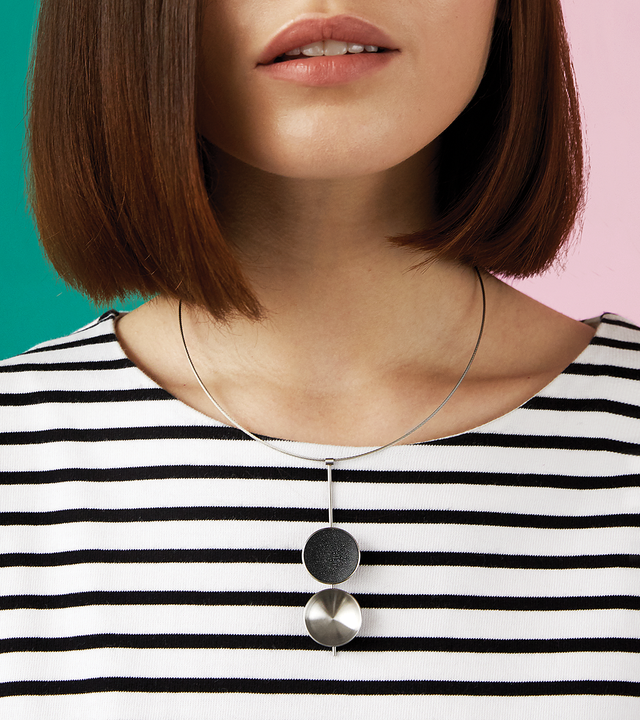 Close-up of the Bauhaus inspired Freya necklace featuring two larger double stainless steel domes, one lined with the sparkle of diamond dust infused black concrete both architecturally supported by an elegant hanging steel post and cable.
