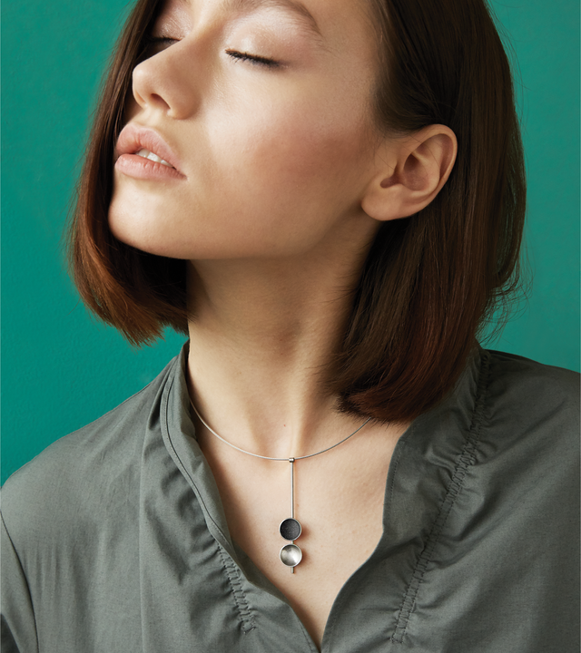 The Bauhaus inspired Freya Minor necklace features two double stainless steel domes, one lined with diamond dust infused black concrete both architecturally supported by an elegant hanging steel post.