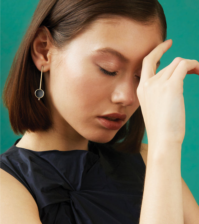 a model wearing A pair of 14k gold earrings with black concrete lined gold domes and diamond dust accents.