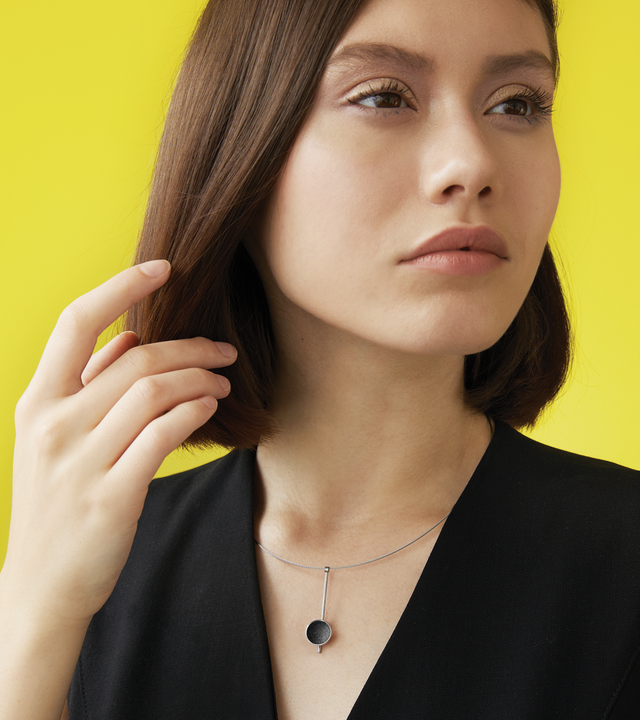 Inspira Minor minimalist necklace sparkle with diamond dust and black concrete set into a stainless steel dome suspended on top of an elegant steel post.