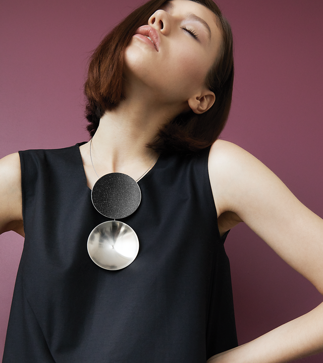 The Ligo Max statement necklace features two stainless steel domes, one lined with diamond dust infused black concrete both supported a vertically hanging steel post.