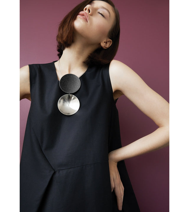 The Bauhaus design inspired Ligo Max statement necklace features two stainless steel domes, one lined with diamond dust infused black concrete both supported a vertically hanging steel post.
