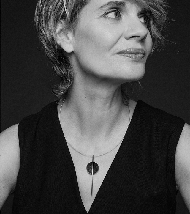 The minimalist Infini necklace sparkles with diamond dust and black concrete set into a stainless steel dome architecturally suspended onto an intersecting steel post.