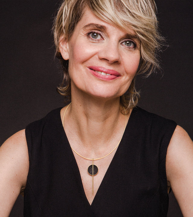 A woman wearing a black dress and a necklace with a geometric design consisting of a black-tinted concrete dome with diamond dust and a vertical linear element.