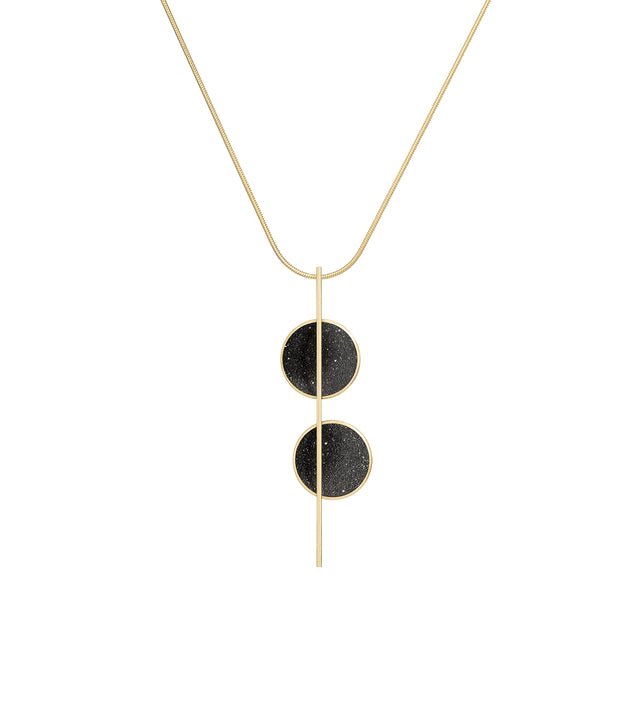 A Bauhaus inspired, elegant necklace with two solid 14k gold circular domes asymmetrically intersected by a vertical gold bar, with black-tinted concrete pendants.