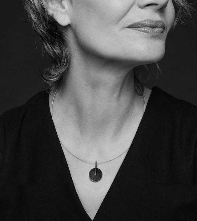This elegant necklace features a diamond dust-encrusted concrete dome in stainless steel with a sleek vertical bar design that creates sophisticated geometric balance. The compact size makes it perfect for everyday layering or standalone wear, while the sparkle of diamond dust against the dark concrete offers subtle luxury that catches the light beautifully. Suspended on a delicate snake chain, this lightweight piece combines industrial materials with refined craftsmanship for effortless contemporary style.