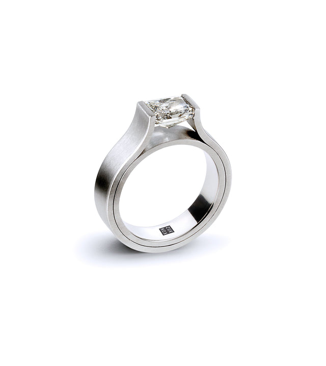 A 1ct emerald cut diamond set horizontally in a platinum ring with a simple design.