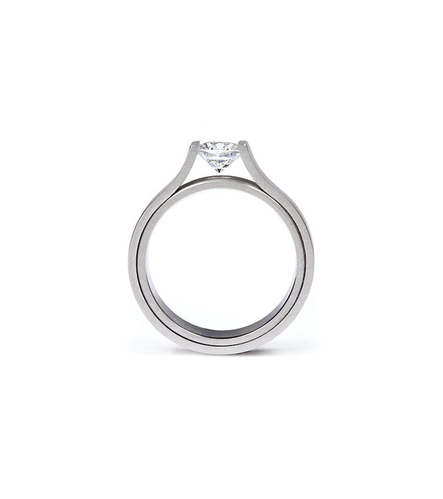 This ring showcases a striking minimalist design, featuring a half-carat diamond elegantly suspended within a sculptural band. Its clean, modern form highlights precision craftsmanship and architectural balance. Available in stainless steel, platinum, or a platinum and gold combination, this piece embodies refined simplicity and timeless strength. floating diamond