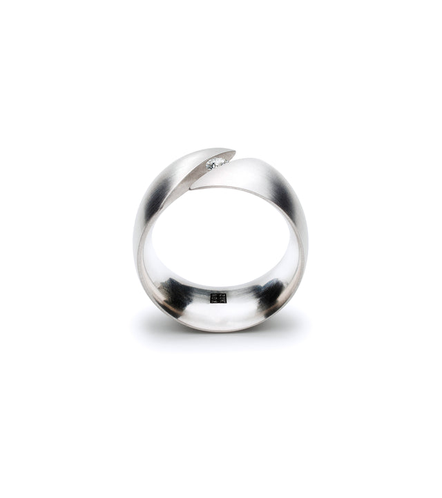 This distinctive ring features a substantial curved band in platinum or stainless steel with a bold split design that securely holds a .10-carat diamond in a modern tension setting. The sculptural form creates visual intrigue as the metal wraps smoothly around the finger, with the opening drawing attention to the diamond's brilliant sparkle at the center. The brushed finish adds contemporary sophistication while the generous proportions offer comfortable everyday wear with confident presence.