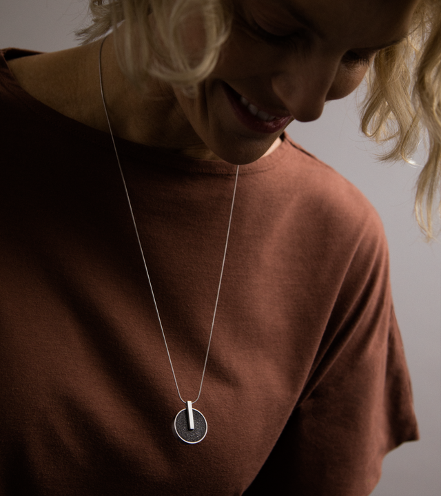 Model wearing a circular stainless steel locket set with diamond dust infused black concrete.