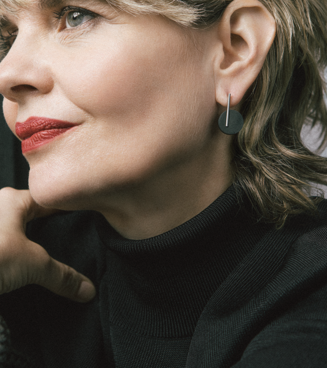 Model wears smaller music-note-like earrings in black concrete.